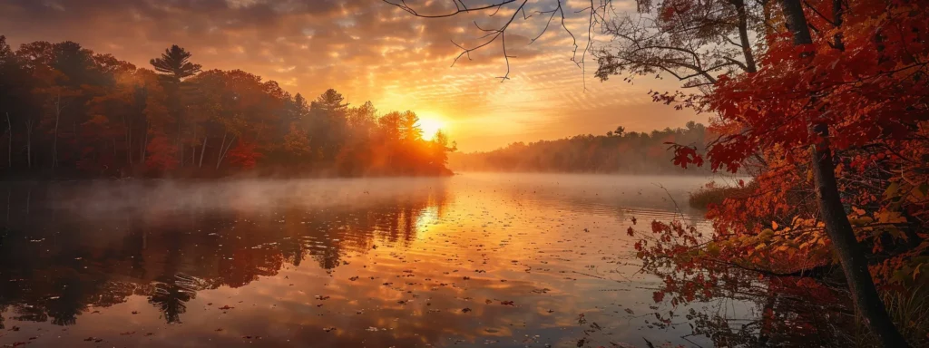 a majestic sunrise casts golden light over a tranquil lake, where mist gently rises from the shimmering water, surrounded by vibrant autumn foliage in vivid reds and oranges.